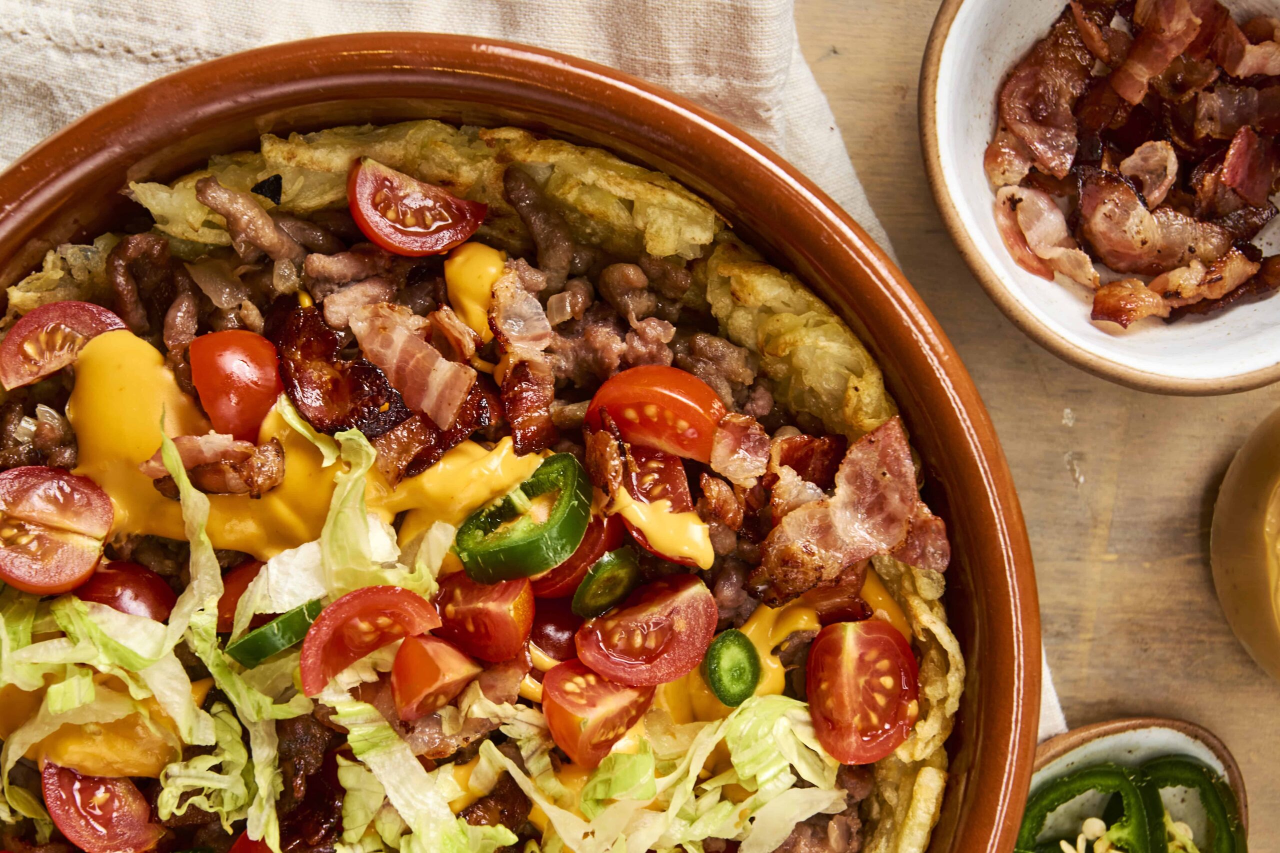 Savory homemade taco casserole with crispy tortillas, melted cheese, cherry tomatoes, and fresh lettuce in a rustic clay dish. Perfect comfort food for Taco Tuesday or family dinner.