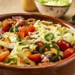 Fresh vegetable salad with cherry tomatoes, cucumbers, lettuce, and sliced peppers in a rustic ceramic bowl. Perfect for healthy eating and meal ideas.