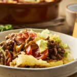 Sizzling beef and vegetable stir-fry with tomatoes and lettuce in a white bowl, served with sliced green chili peppers and a glass jar of creamy mustard sauce, delicious home-cooked Asian-inspired meal, focus on fresh ingredients and vibrant colors.
