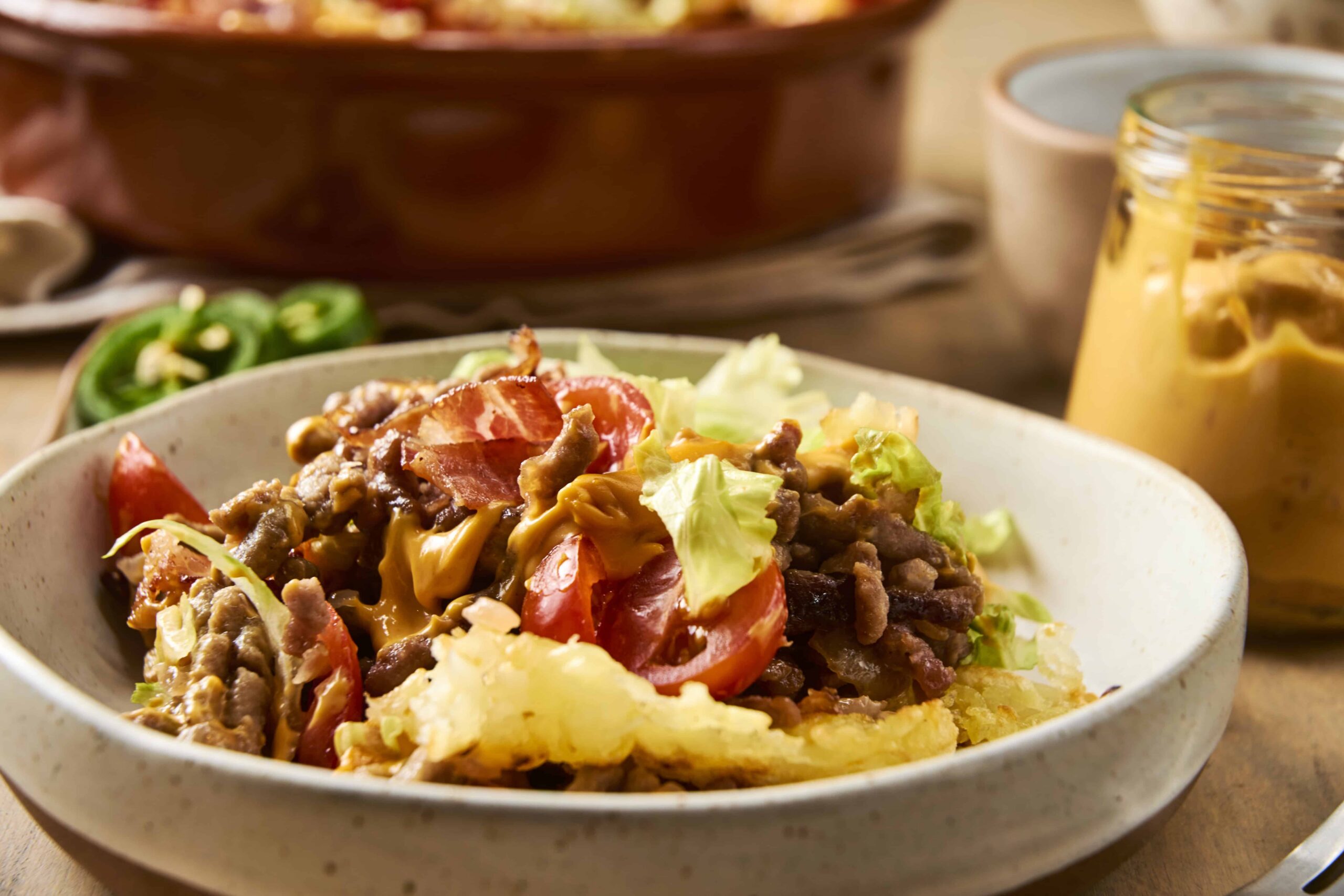 Sizzling beef and vegetable stir-fry with tomatoes and lettuce in a white bowl, served with sliced green chili peppers and a glass jar of creamy mustard sauce, delicious home-cooked Asian-inspired meal, focus on fresh ingredients and vibrant colors.