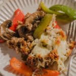 Sautéed mushrooms, ground meat, roasted bell peppers, green chili pepper, and cheesy baked potato casserole served on a white ribbed plate.
