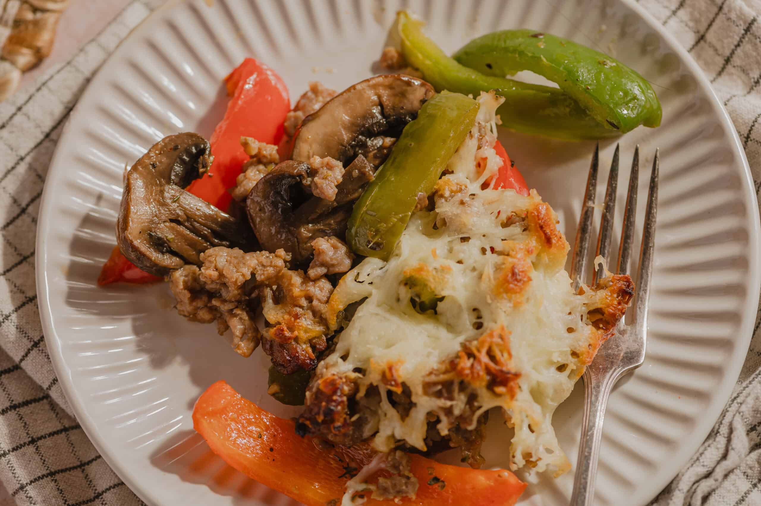 Sautéed mushrooms, ground meat, roasted bell peppers, green chili pepper, and cheesy baked potato casserole served on a white ribbed plate.
