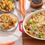 Creamy baked pasta casserole with ground beef, vegetables, and cheese garnished with green onions on a white tablecloth, surrounded by pasta bowls, carrots, and spices.