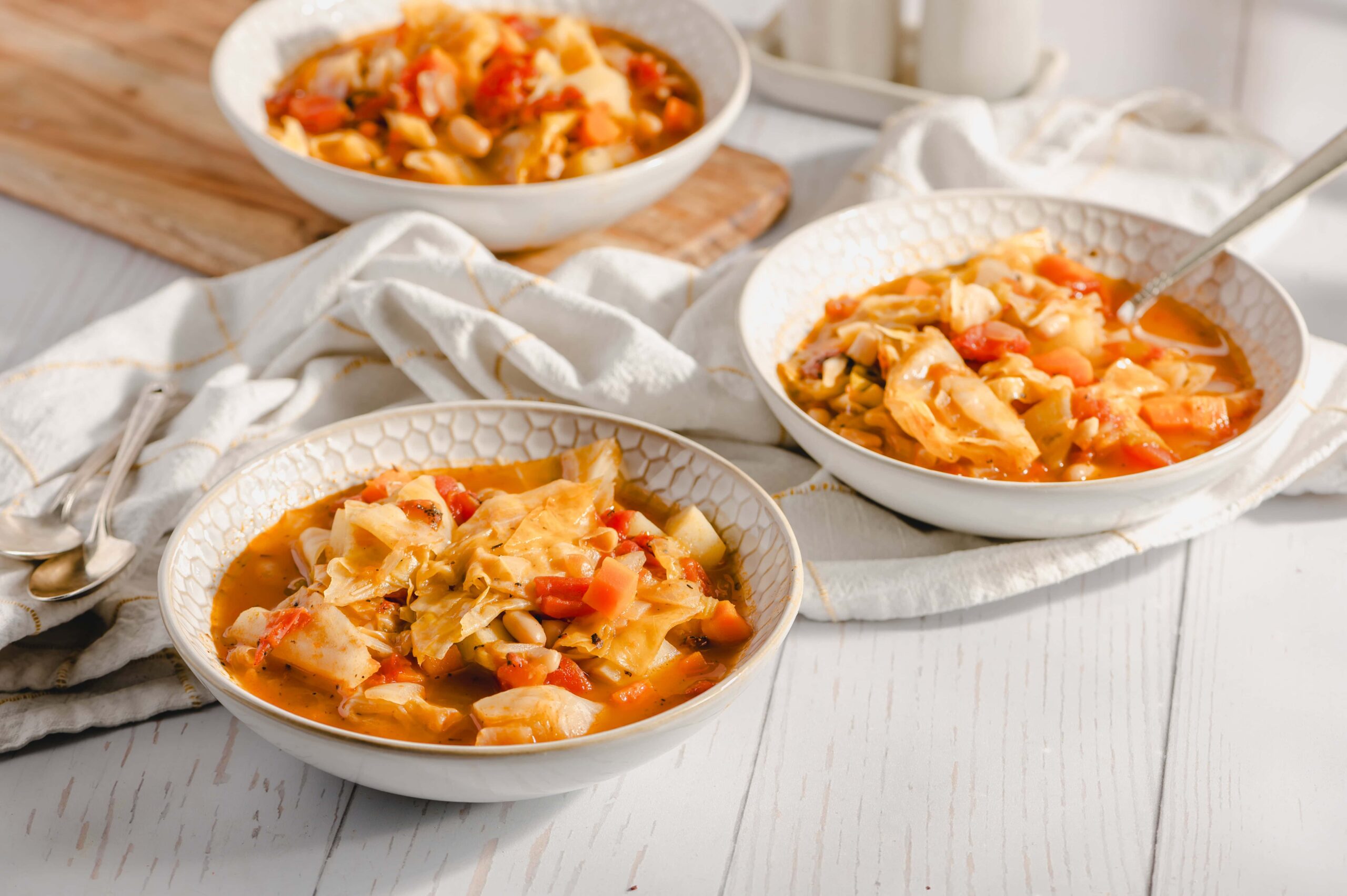Creamy homemade cabbage soup with beans and vegetables served in white patterned bowls, perfect for a comforting meal.