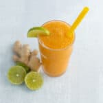 Refreshing ginger lime orange smoothie with lime wedge and yellow straw on light background, healthy fruit smoothie recipe, vibrant citrus beverages, summer drinks, and fresh ingredients.