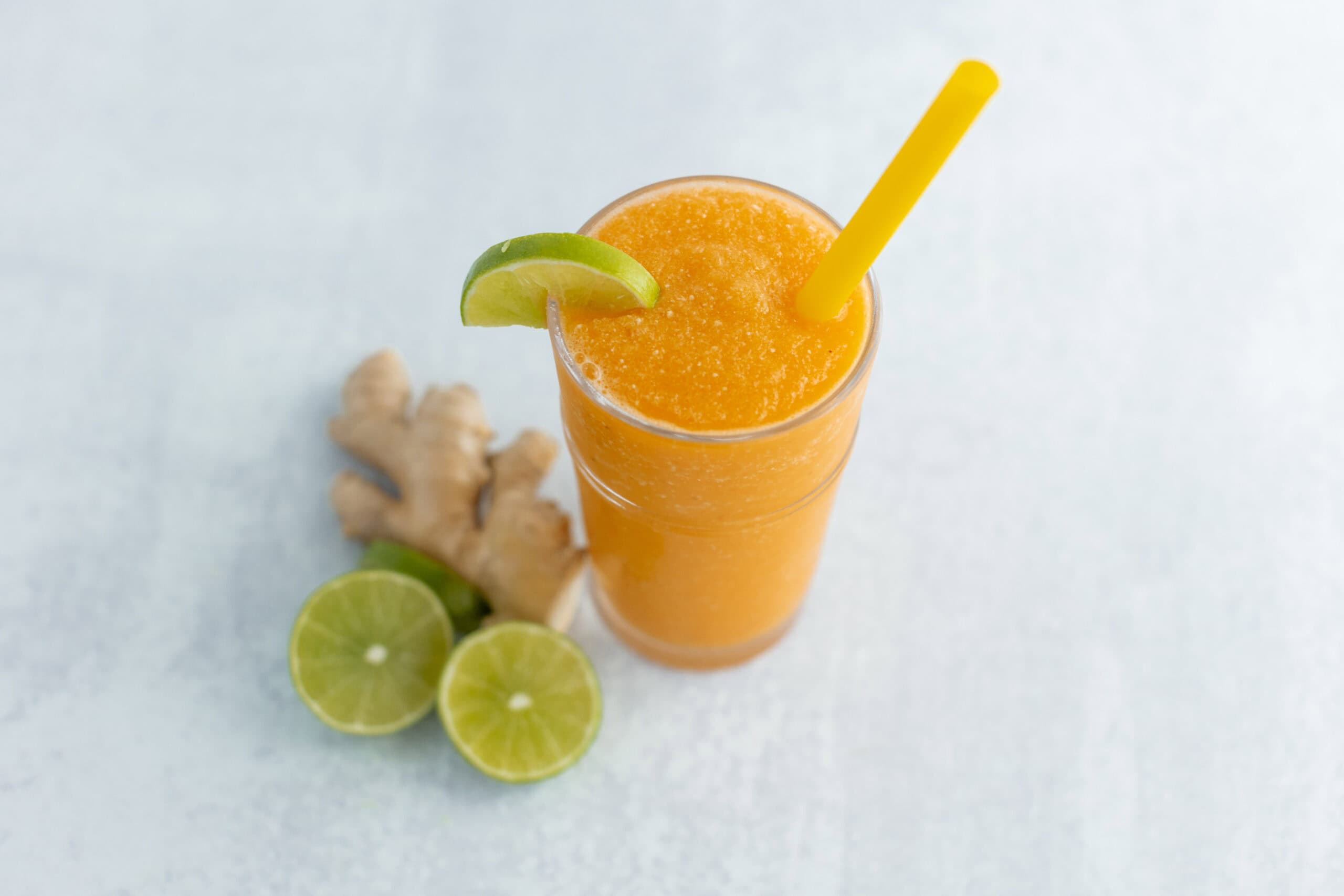 Refreshing ginger lime orange smoothie with lime wedge and yellow straw on light background, healthy fruit smoothie recipe, vibrant citrus beverages, summer drinks, and fresh ingredients.