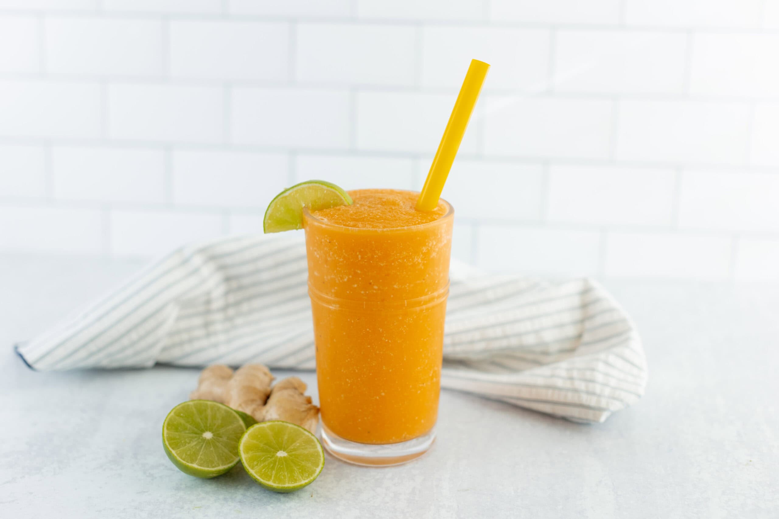 Fresh mango and lime smoothie garnished with lime wedge and served with ginger on a white surface. Perfect for a healthy, refreshing drink recipe.