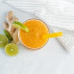 Refreshing orange smoothie with lime garnish, served with a yellow straw on a light surface.