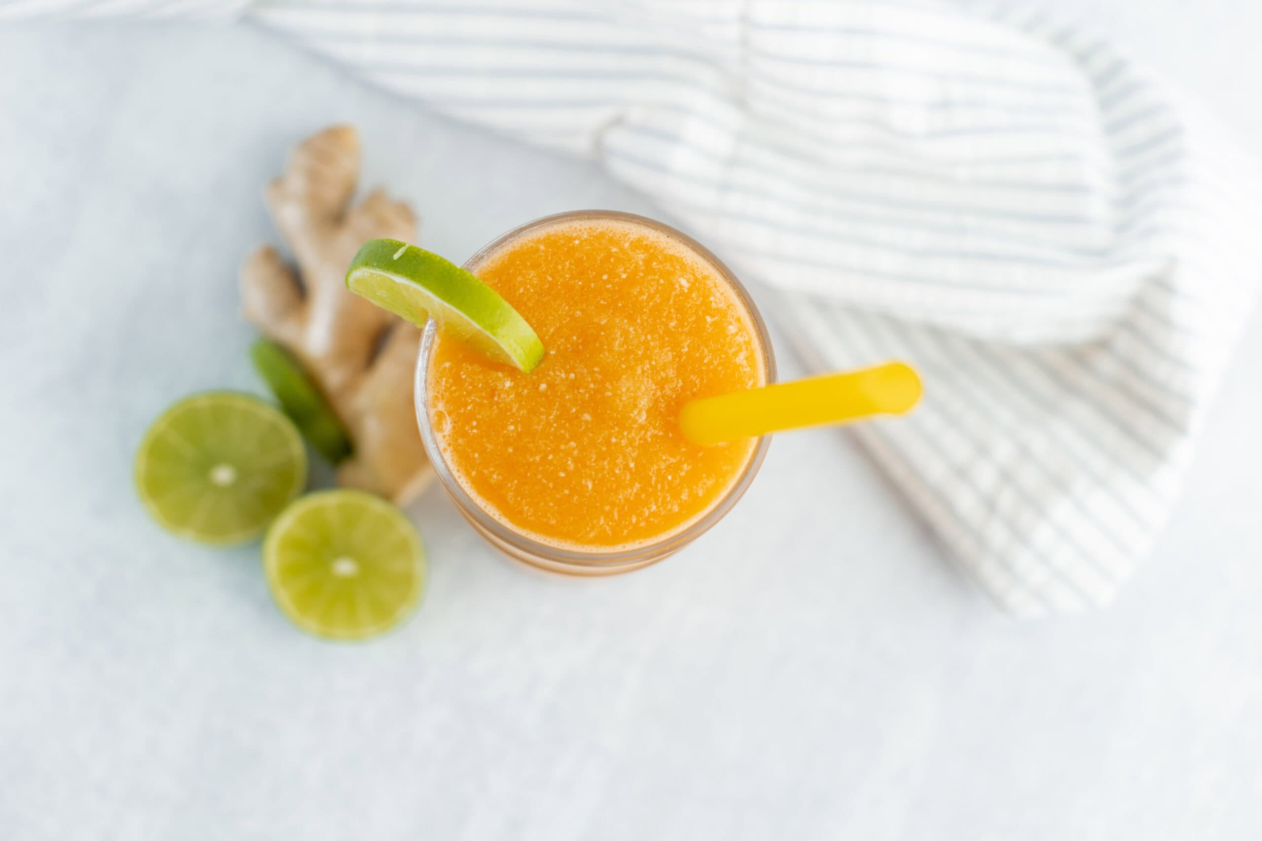 Refreshing orange smoothie with lime garnish, served with a yellow straw on a light surface.
