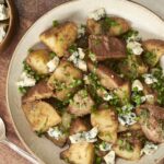 Savory potato hash topped with crumbled blue cheese and chopped green onions, served on a rustic plate, perfect for breakfast or brunch.