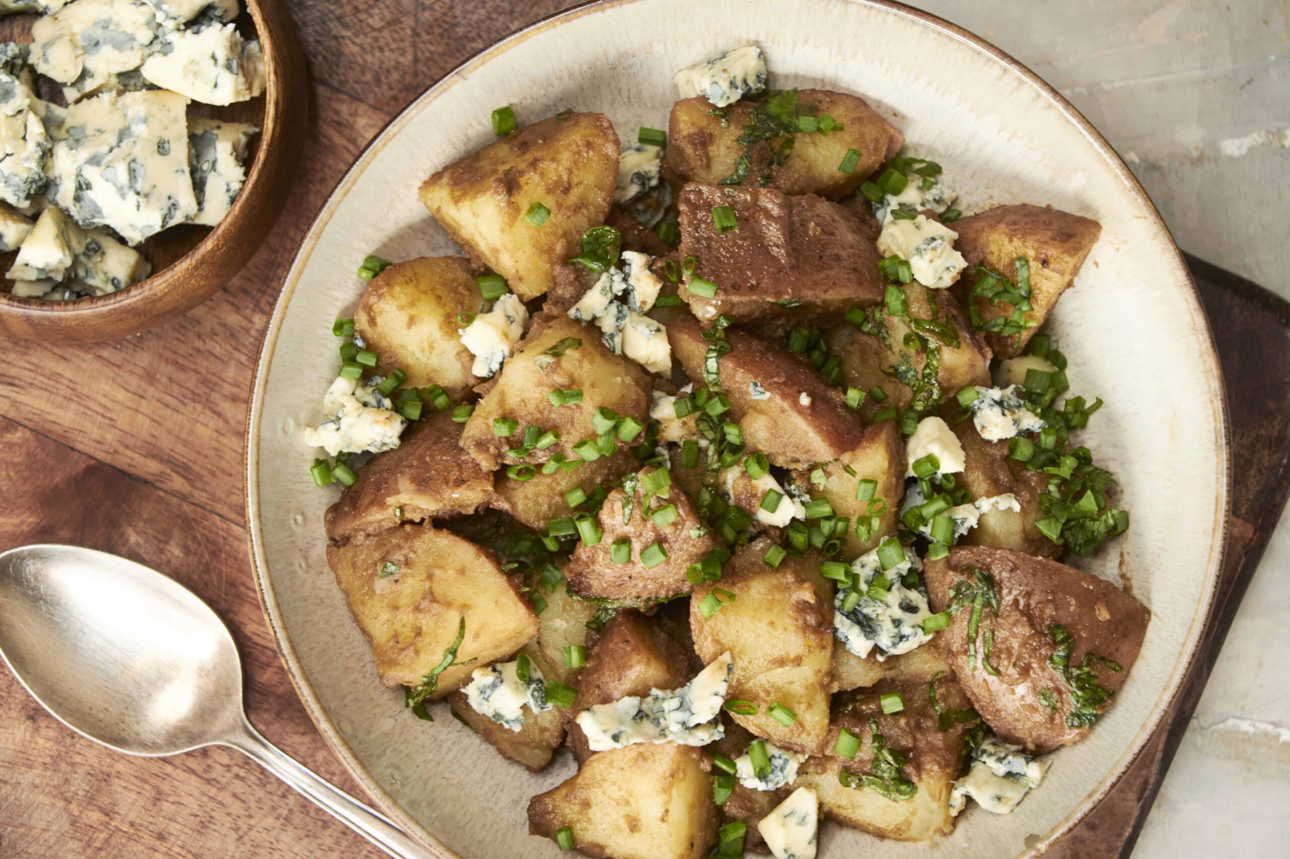 Savory potato hash topped with crumbled blue cheese and chopped green onions, served on a rustic plate, perfect for breakfast or brunch.