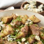 Golden roasted potatoes topped with blue cheese crumbles and chopped green onions in a rustic bowl.