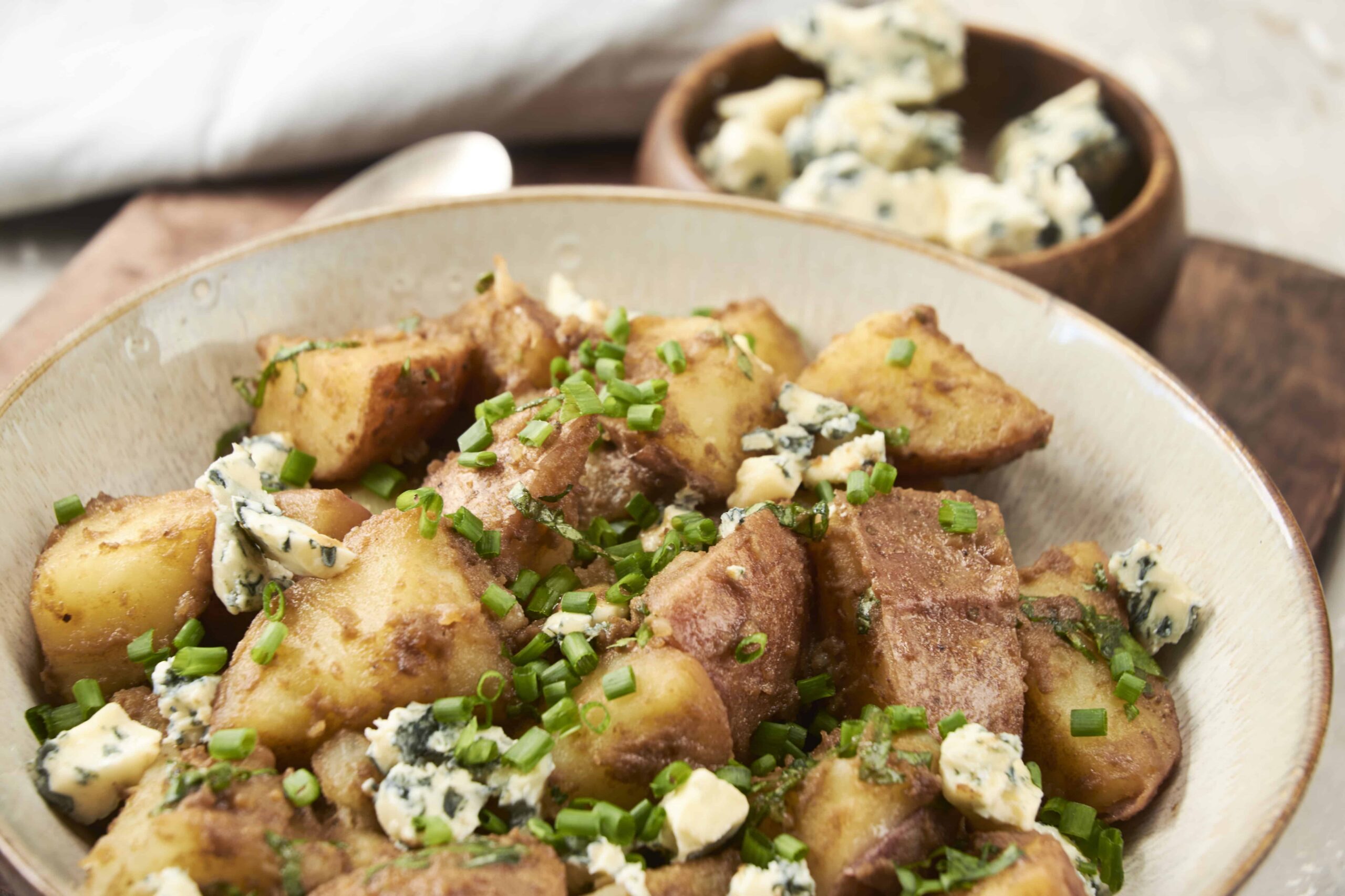 Golden roasted potatoes topped with blue cheese crumbles and chopped green onions in a rustic bowl.