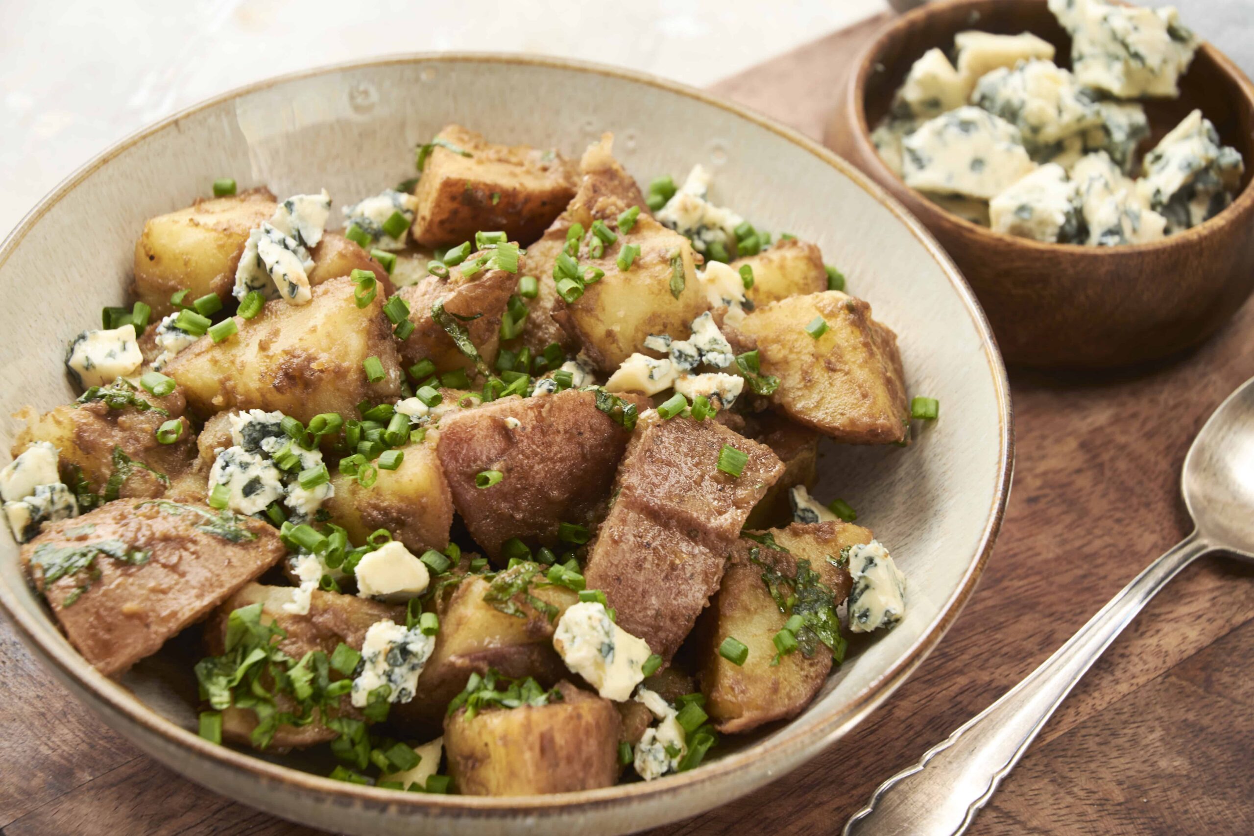 Golden roasted potatoes topped with crumbled blue cheese and chopped fresh chives, served in a rustic bowl for a hearty and flavorful side dish or appetizer.