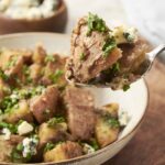 Creamy beef stroganoff with tender potatoes, garnished with fresh chives and blue cheese crumbles. Perfect comfort food recipe with rich, savory flavors.