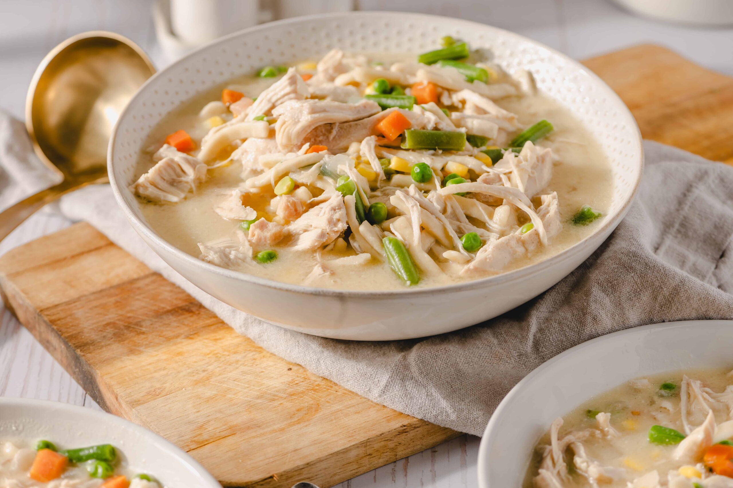 Tender chicken and mixed vegetables in a creamy broth, served in white bowls, perfect for comfort food and healthy eating, featuring carrots, green beans, peas, corn, and shredded chicken.