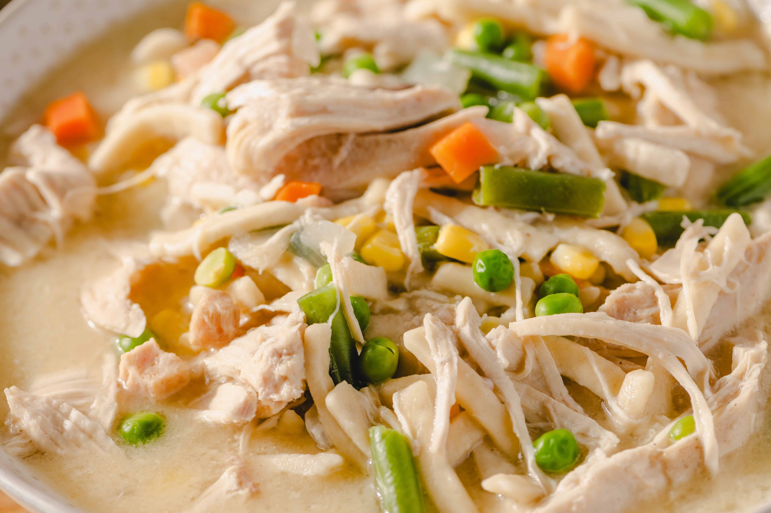 Creamy chicken and vegetable soup with shredded chicken, peas, carrots, and green beans in a rich broth, perfect for cozy homemade meals and easy to prepare.