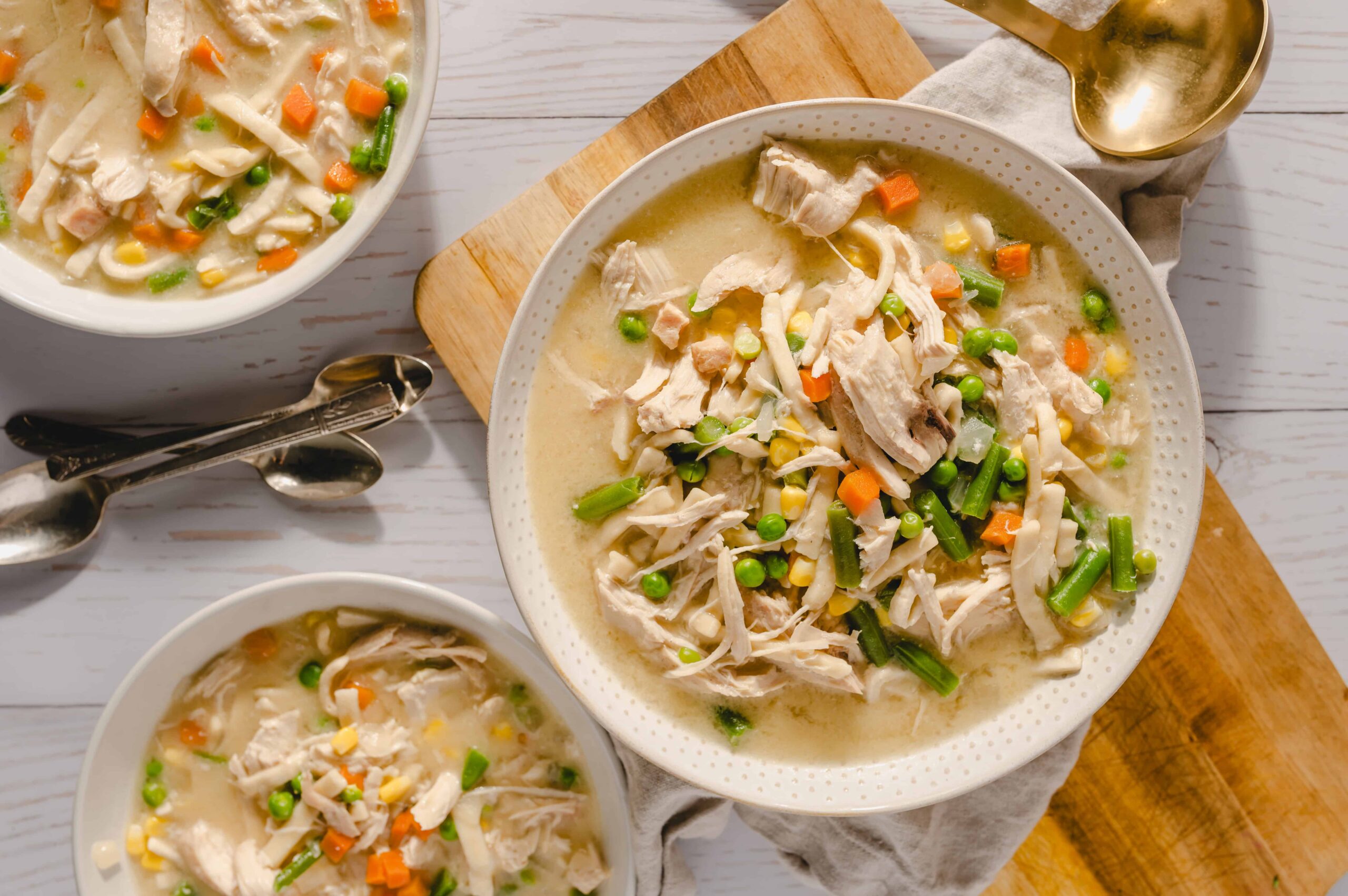 Creamy chicken vegetable soup with shredded chicken, carrots, peas, corn, and green beans served in white bowls. Perfect comfort food for cold days, rich in flavors, and easy to prepare.