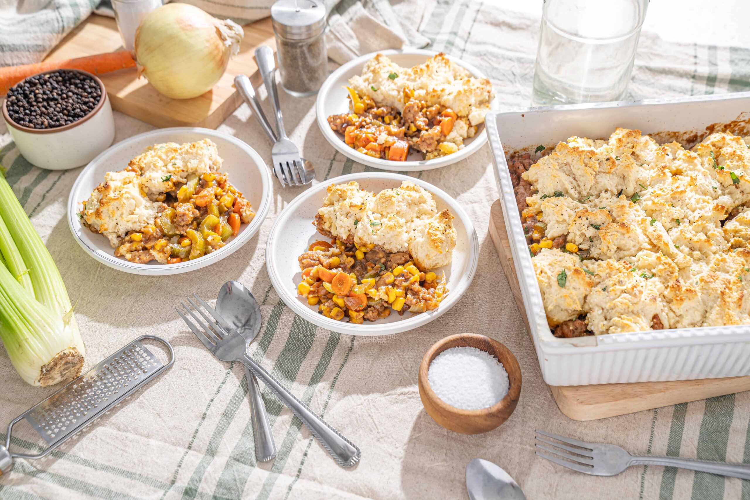 Creamy chicken pot pie with vegetables served in small white bowls on a rustic table with fresh ingredients and kitchen utensils.