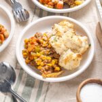 Creamy cheesy mashed potatoes served with hearty beef and vegetable stew on white plates, cozy rustic table setting, perfect comfort food, home-cooked meal, warm and inviting.