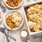 Creamy shepherd's pie topped with mashed potatoes, served alongside vegetable beef stew in white bowls, garnished with herbs. Perfect comfort food for family dinners.