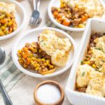 Hearty shepherd's pie with mashed potatoes, ground beef, mixed vegetables, and herbs served in baked casserole dishes. Perfect comfort food recipe for family dinners.
