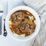 Savory mushroom pot roast served with mashed potatoes on a white plate, garnished with herbs, close-up view, top-down angle.