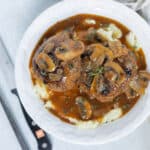 Savory meatballs with mushroom gravy served over mashed potatoes in a white bowl, garnished with fresh herbs, perfect for comfort food recipes.