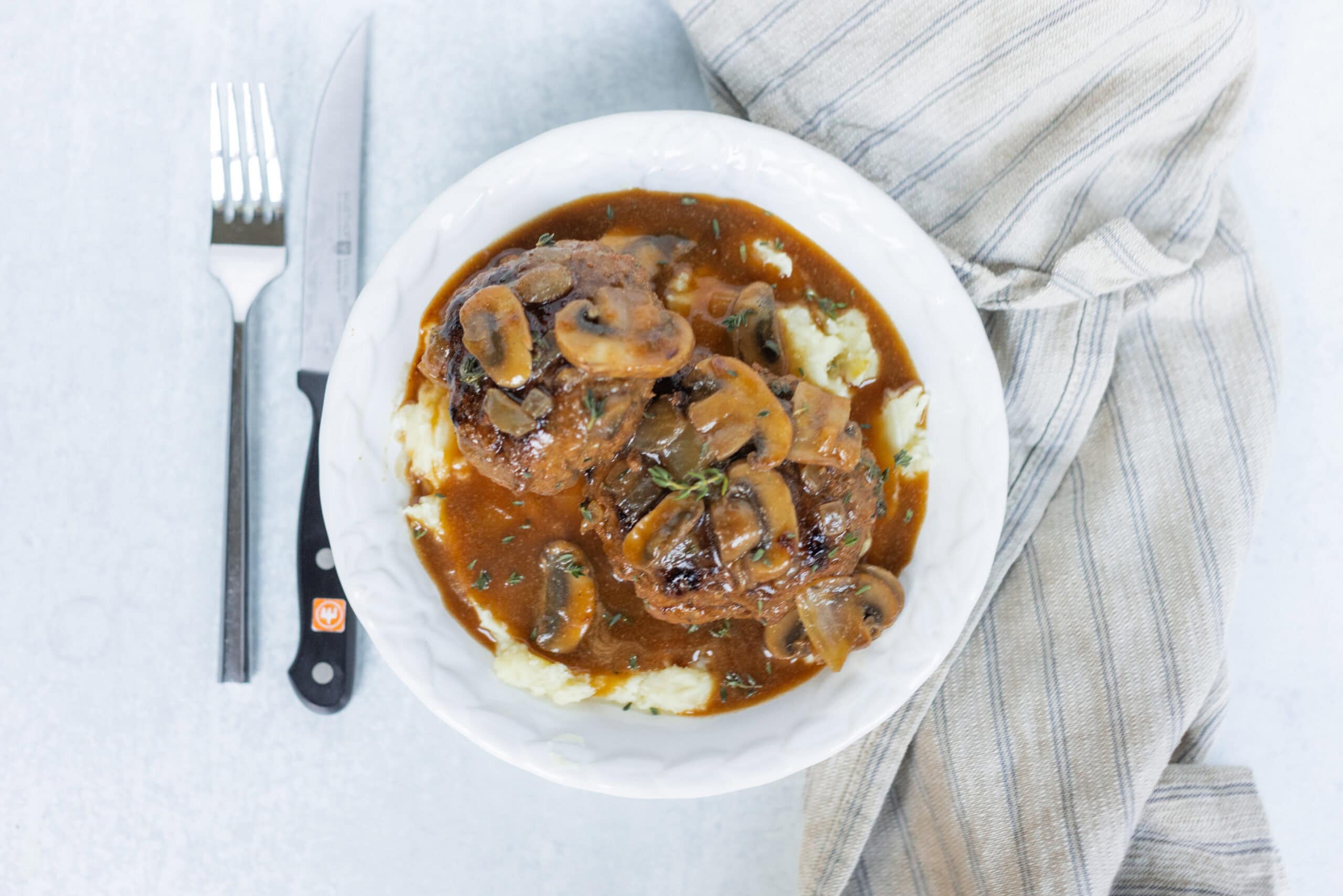 Savory mushroom pot roast served with mashed potatoes on a white plate, garnished with herbs, close-up view, top-down angle.