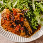 Grilled chicken breast topped with savory mango salsa on a white plate with mixed greens and leafy salad; healthy and flavorful dinner recipe.