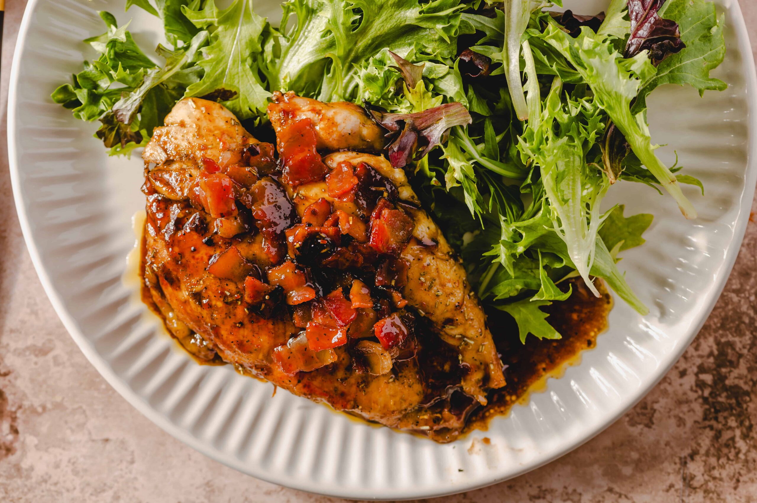 Grilled chicken breast topped with savory mango salsa on a white plate with mixed greens and leafy salad; healthy and flavorful dinner recipe.