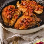 Tender chicken thighs in a rich, savory sauce with chopped tomatoes, served in a white baking dish, garnished with fresh herbs, perfect for a hearty meal, featured on Hey Recipe.