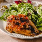 Savory chicken thigh topped with rich mushroom and wine sauce served with fresh mixed green salad on a white plate. Perfect for a flavorful and healthy meal option.
