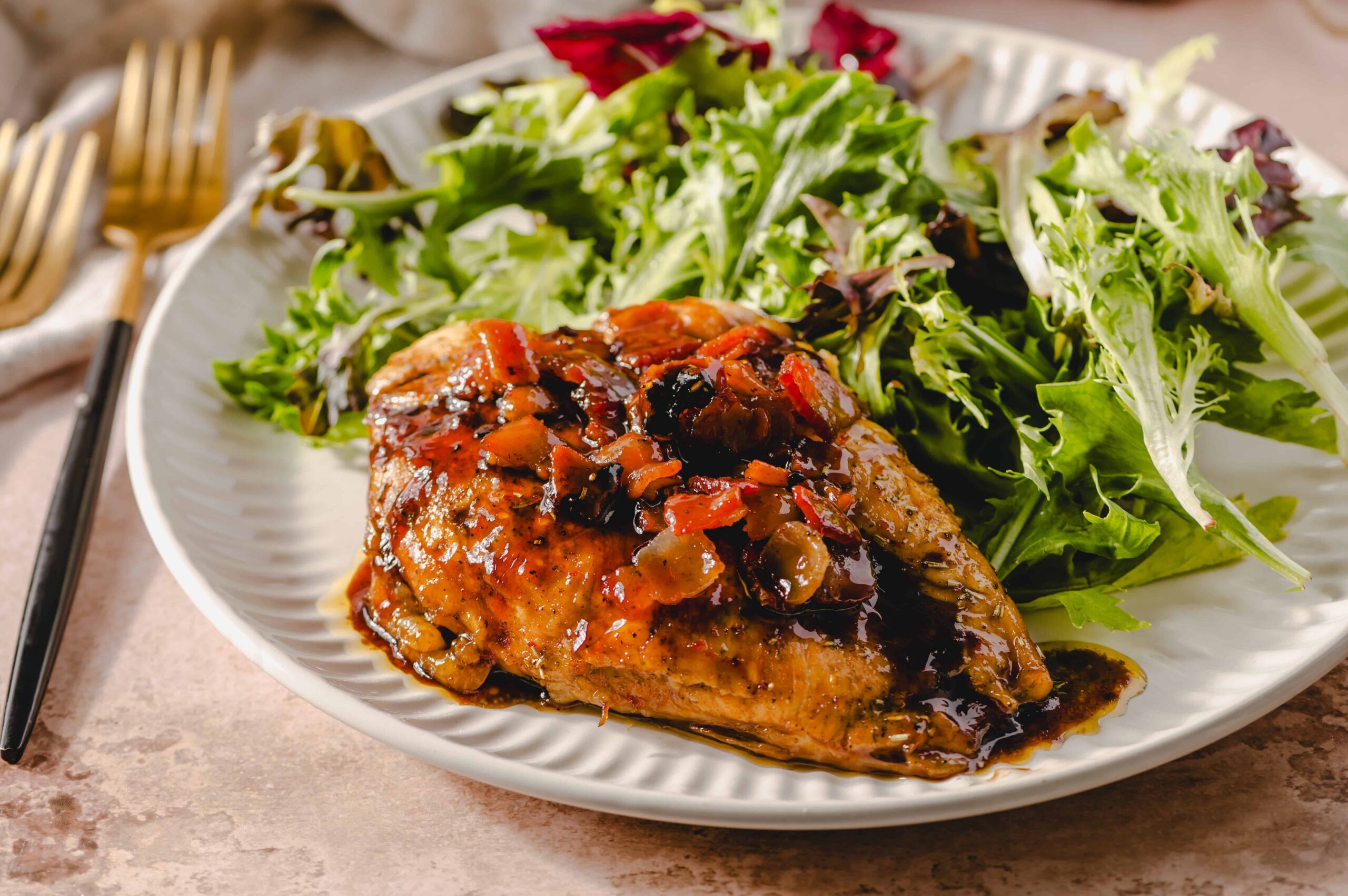Savory chicken thigh topped with rich mushroom and wine sauce served with fresh mixed green salad on a white plate. Perfect for a flavorful and healthy meal option.
