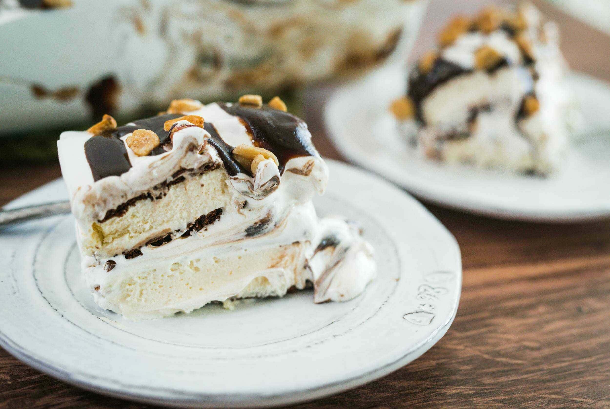 Layers of vanilla and chocolate cake with whipped cream, chocolate drizzle, and chopped nuts, beautifully plated on a white dish, perfect for dessert or celebration.