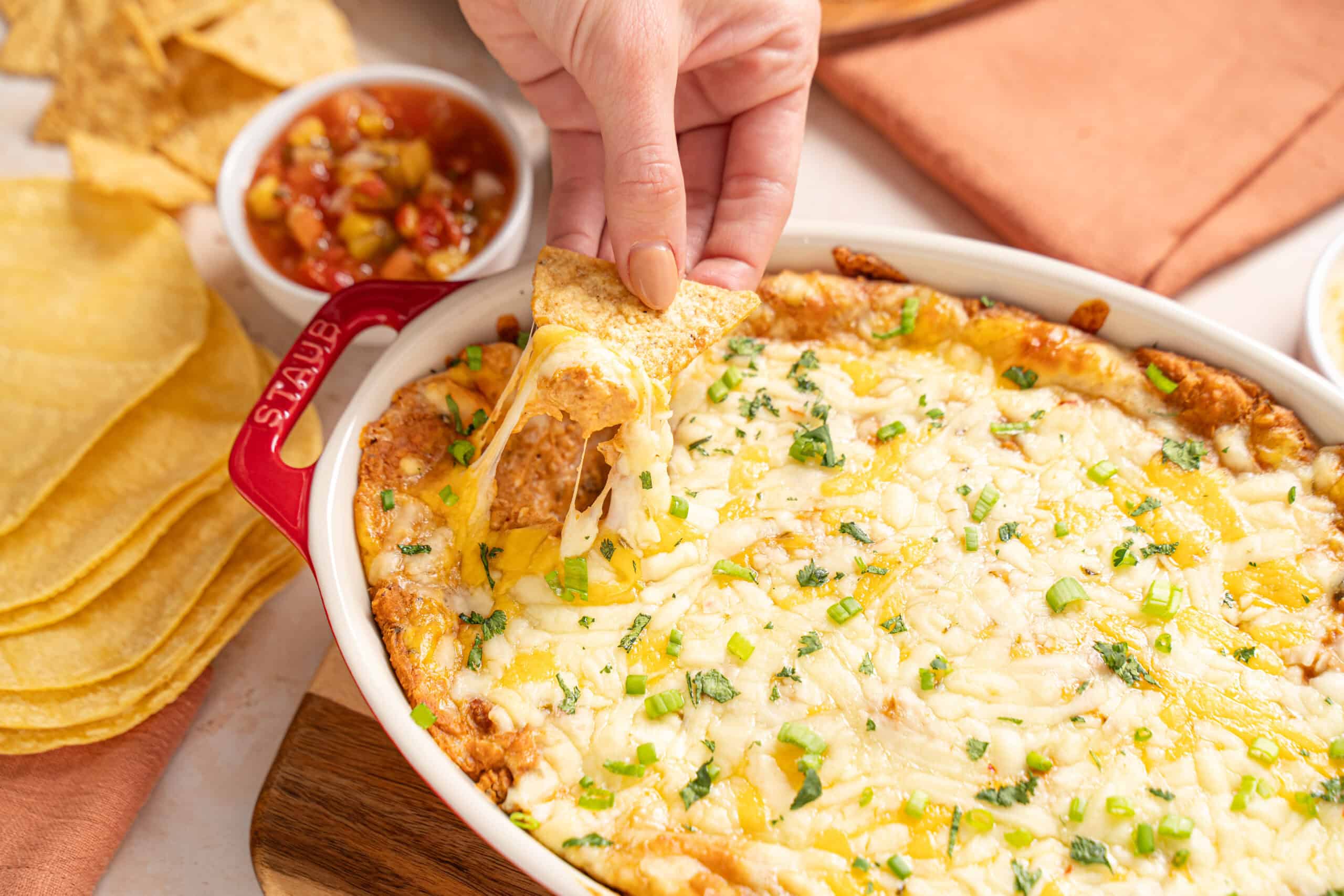 Creamy cheesy baked Mexican dip with melted cheese, ground beef, and fresh green herbs served with crispy tortilla chips.