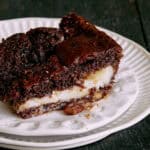 Decadent pecan pie with a rich, chocolate topping served on a vintage white plate with a gold fork on a dark rustic surface. Perfect dessert for holiday celebrations or sweet cravings.