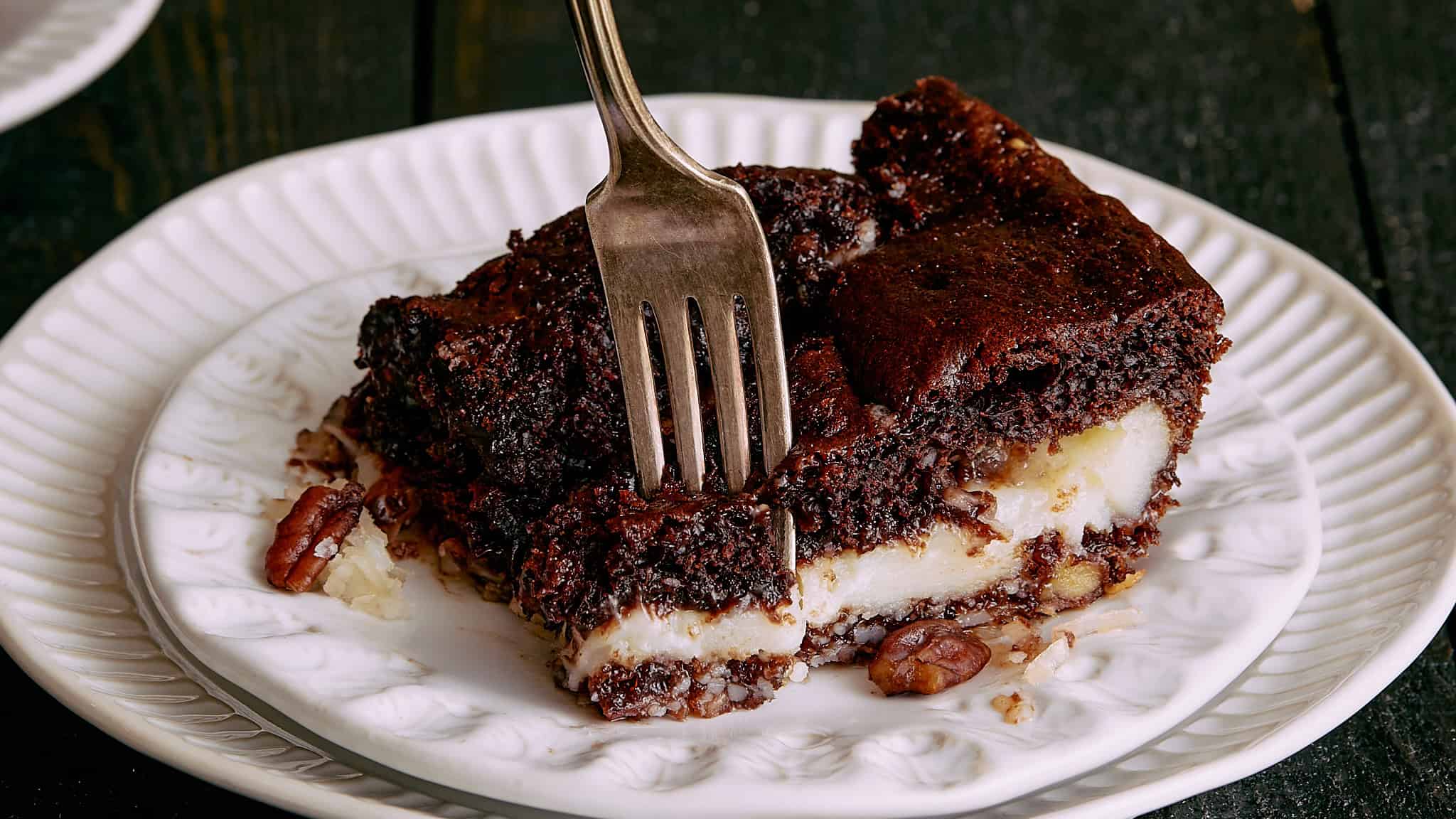 Rich, indulgent chocolate pecan pie with a flaky crust and gooey filling served on a decorative white plate. Perfect for dessert, bakers and chocolate lovers.