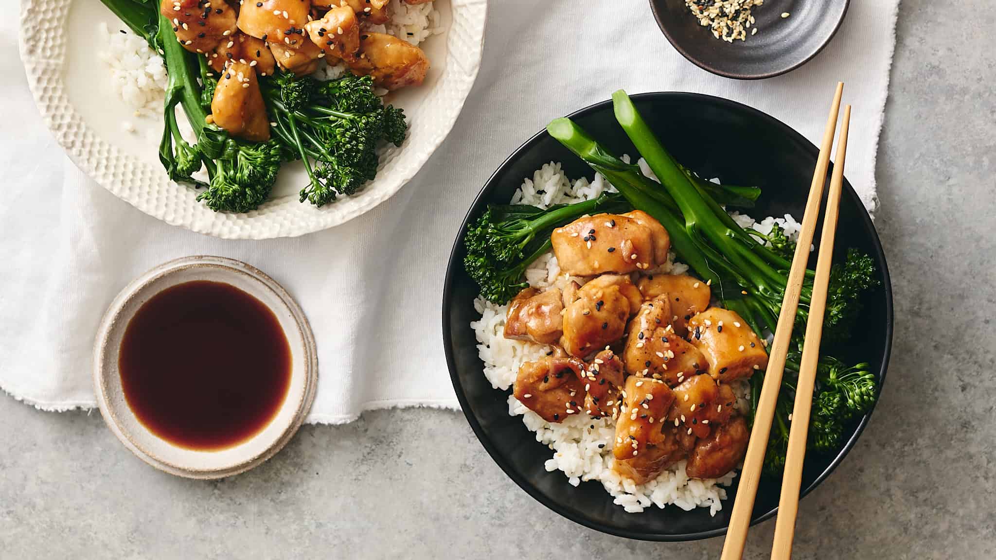 Succulent teriyaki chicken served over fluffy white rice with sautéed greens and broccoli, accompanied by soy sauce in a small bowl, perfect for a delicious Asian-inspired meal.