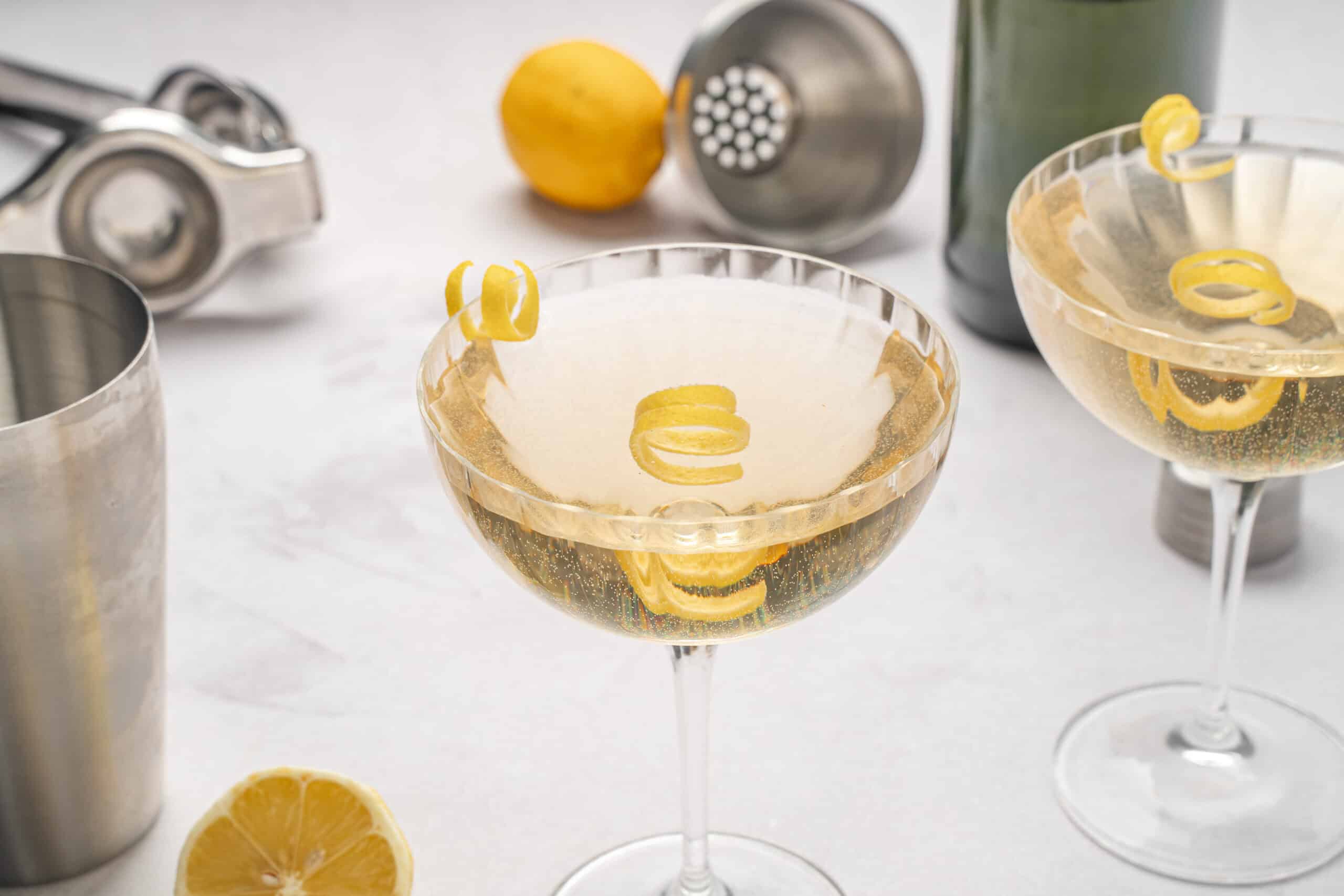 Chilled lemon-flavored cocktail with lemon twists in elegant glassware, surrounded by cocktail tools and fresh lemon slices for a refreshing drink experience.