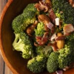 Steamed broccoli topped with crispy bacon, garlic, and cashews served in a wooden bowl, highlighting a healthy and flavorful vegetable dish.