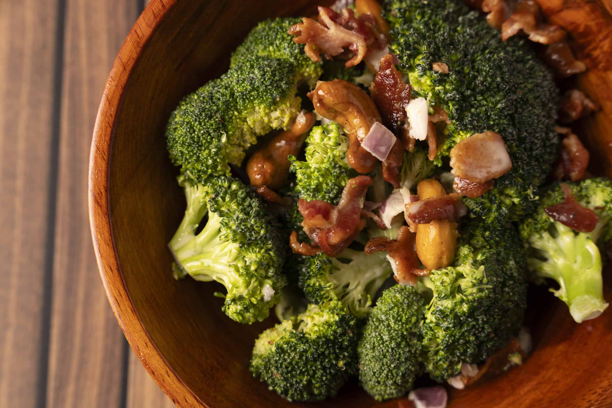 Steamed broccoli florets topped with crispy bacon bits, cashew nuts, and a savory sauce, served in a wooden bowl. A healthy and delicious vegetable dish perfect for lunch or dinner.