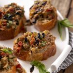 Savory stuffed mushroom caps topped with black sesame seeds and fresh herbs, served on a white platter with a striped cloth, perfect for appetizer recipes and party snacks.
