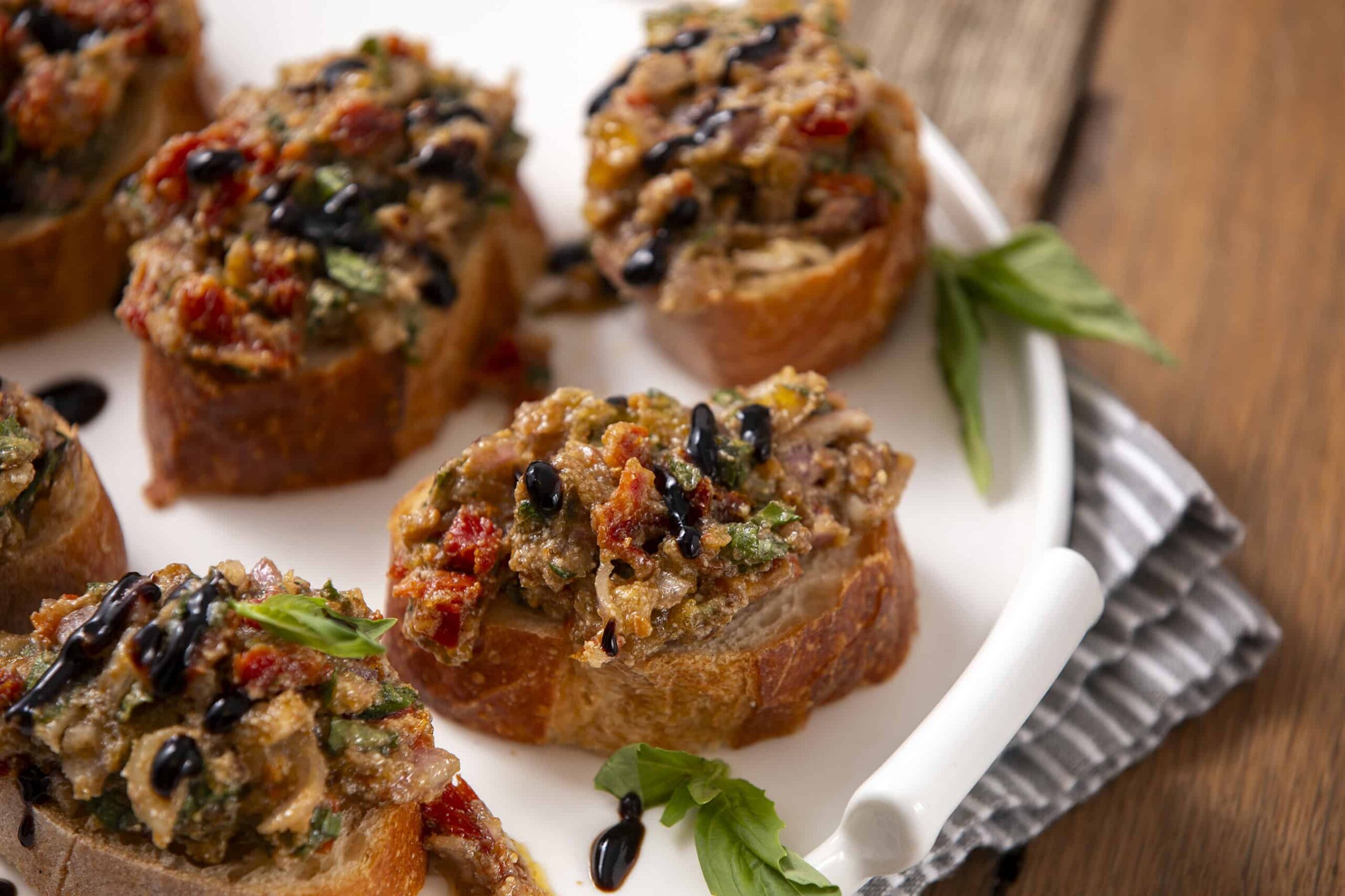 Savory stuffed mushroom caps topped with black sesame seeds and fresh herbs, served on a white platter with a striped cloth, perfect for appetizer recipes and party snacks.