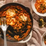 Savory baked white beans with tomato sauce and herbs served in a cast iron skillet, rustic wooden table setting, delicious comfort food with cheese melt, hearty and flavorful.