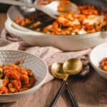Creamy baked bean casserole with melted cheese and herbs served in decorative bowls on rustic wooden table. Perfect comfort food dish for family dinner or outdoor gathering.