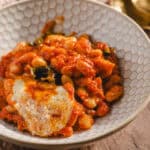 Savory bean and vegetable stew topped with melted cheese served in a textured white bowl, perfect for a hearty meal or comfort food.