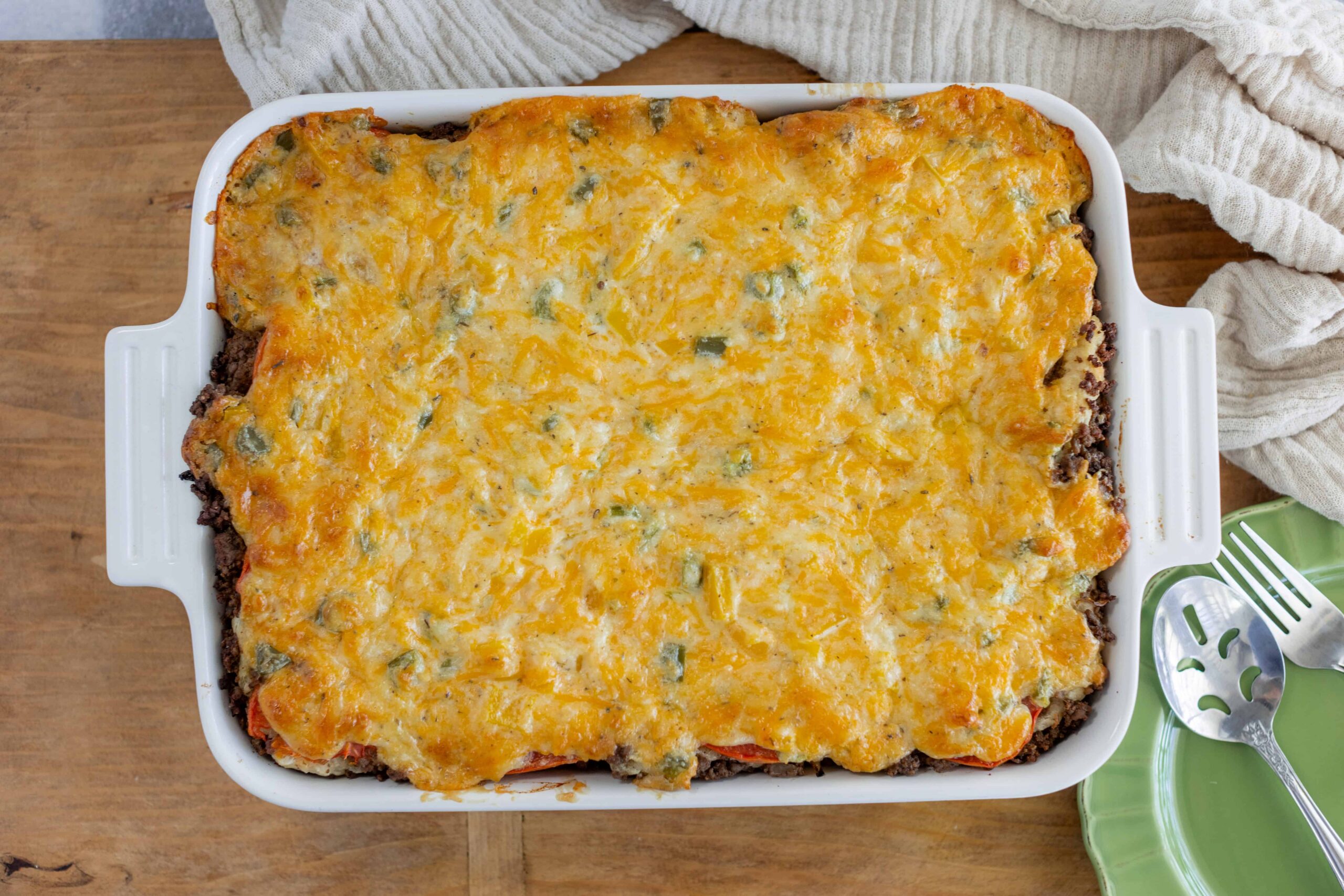Golden baked cheesy casserole with ground beef and vegetables in a white baking dish.