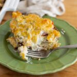 Cheesy breakfast casserole on a green plate with a fork, featuring melted cheese, eggs, and ground beef, served on a wooden table.