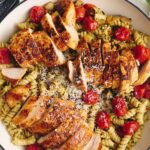 Succulent grilled chicken breast slices served over a pasta salad with cherry tomatoes, shredded cheese, and herbs, garnished for a flavorful dinner.